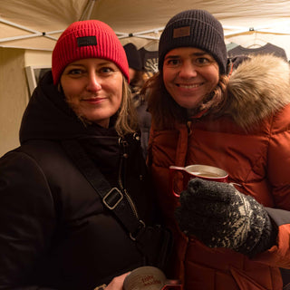 Sabine und Tina, die Gründerinnen von Winecraft, genießen einen Glühwein im Winter – beide tragen unsere Merino Beanies in stylischen Farben.